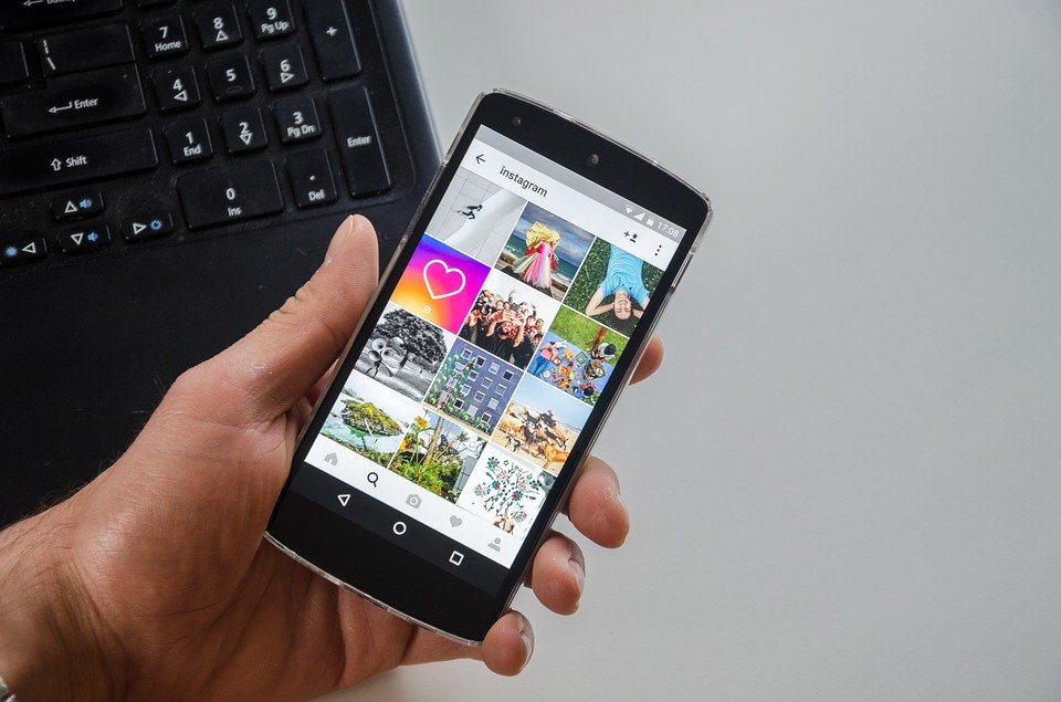Mail hand holding mobile phone and the screen is displaying Instagram feed