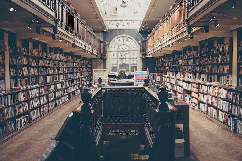 Big Library with shelves full of books on both walls with a down stairs in the center of the room